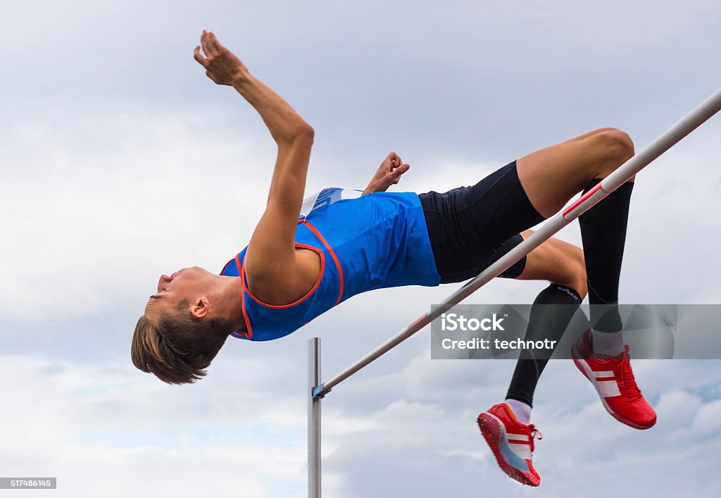 High jump competition in cloudy wheather Side view of young athlete jumping over the lath High Jump Stock Photo