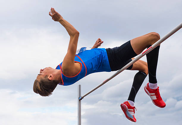 High jump competition in cloudy wheather Side view of young athlete jumping over the lath high jump stock pictures, royalty-free photos & images
