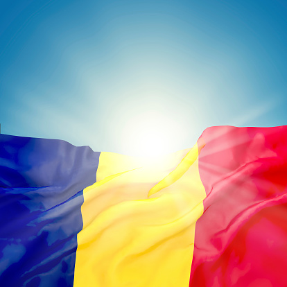 Romanian and Chad official national state flag against peaceful blue sky, rising sun and slight waving on wind