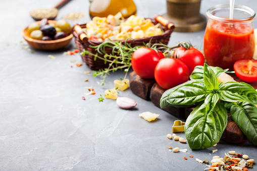 Italian food background with vine tomatoes, basil, spaghetti, olives, parmesan, olive oil, garlic Ingredients on stone table Copy space