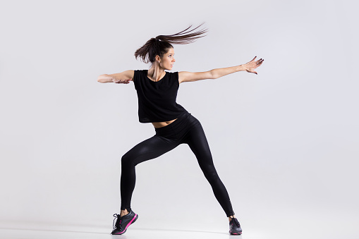 One happy attractive gorgeous young fit modern woman with ponytail working out in sportswear, dancing, full length, studio image on gray background