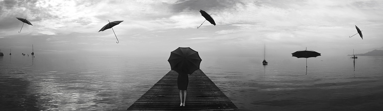 elegant woman repairing from the rain of blacks umbrellas in a surreal landscape sea