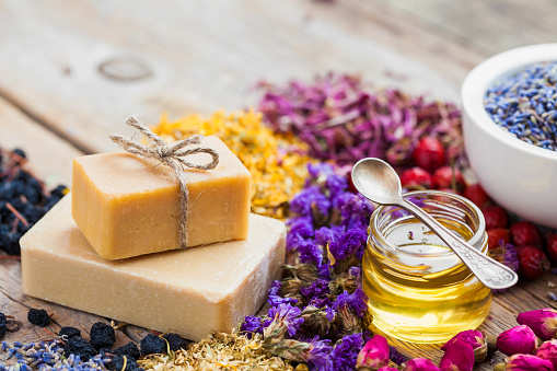 Bars of homemade soaps, honey or oil, heaps of healing herbs and mortar of lavender. Selective focus.