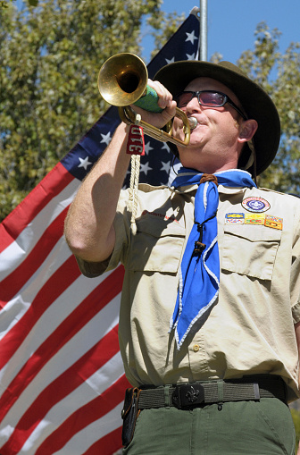 Glendale, CA, USA - September 29, 2013: A man wearing a boy scout uniform stands in front of an American flag playing the bugle at a memorial ceremony in Glendale, California on September 29, 2013.