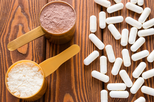 capsules of creatine and protein measuring spoons on a wooden background