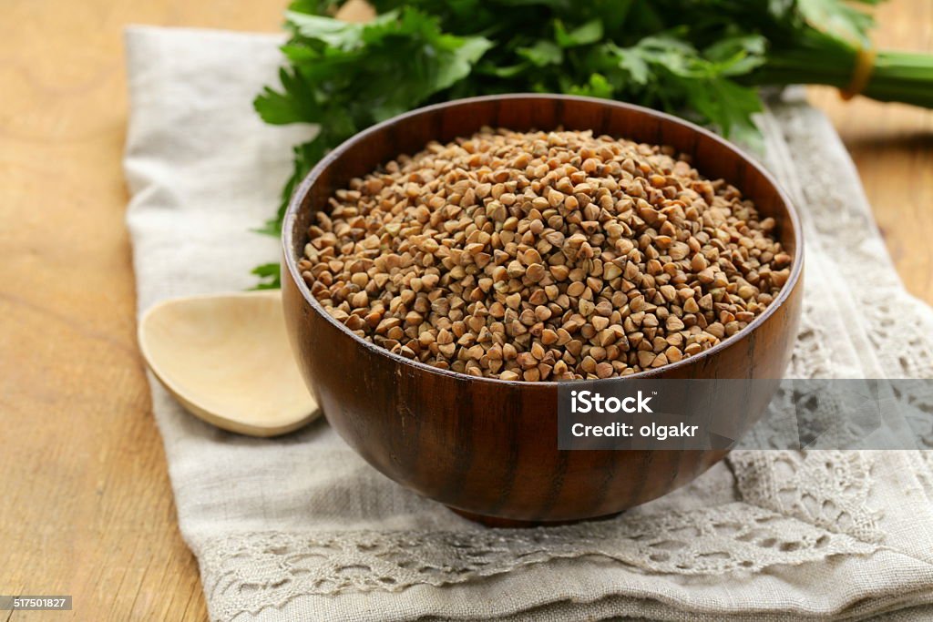 raw de trigo sarraceno groats em uma tigela de madeira sobre a mesa - Foto de stock de Agricultura royalty-free