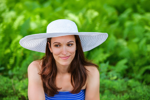 A portrait of a pretty woman smiling outside on a sunny day wearing a sun hat during the summer.  Room for copy space.