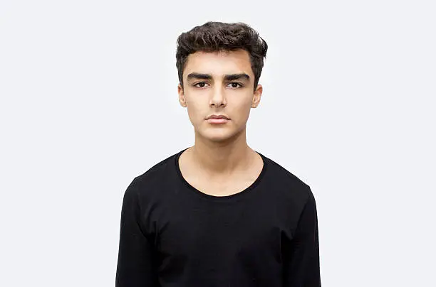 Portrait of teenage boy over white background. Young man standing over isolated on white looking at camera with blank facial expression. Horizontal composition. Image taken in studio and developed from RAW format. Young boy's ethnicity belongs to Turkish, middle eastern ethnicity. He has got short, brown hair.