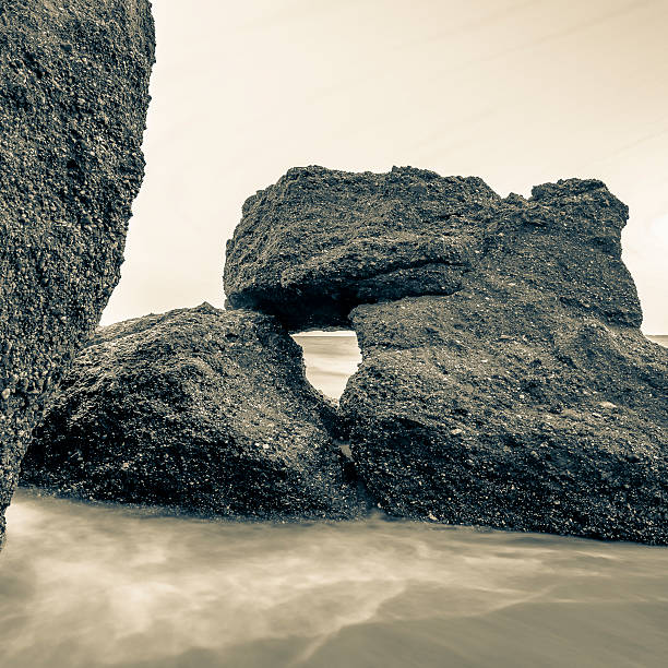 Black and white of boulders which are stacked as nature left them with horizon visible through window in the stone. Long exposure. Square format.