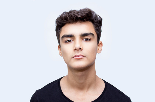 Portrait of teenage boy over white background. Young man standing over isolated on white looking at camera with blank facial expression. Horizontal composition. Image taken in studio and developed from RAW format. Young boy's ethnicity belongs to Turkish, middle eastern ethnicity. He has got short, brown hair.