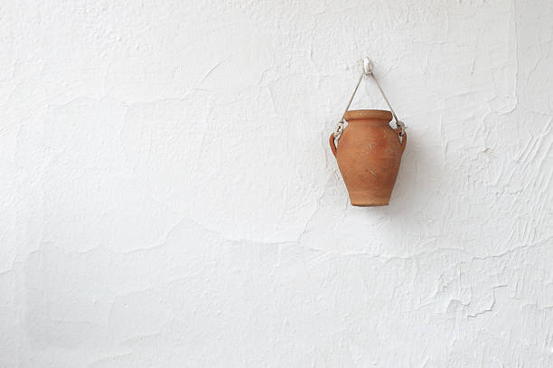 Typical white country house wall in a Mediterranean village with a clay handmade vase hanging from a hock. Empty copy space for editor's text.