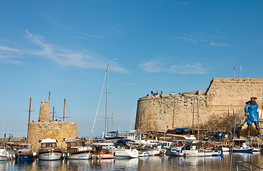 Kyrenia, Cyprus - March 12, 2016: Photo of the waterfront and harbour with sailboats in Kyrenia, Northern Cyprus. People are visiting the harbour for touristic, some of them eating for dinner, some of them are resting near the sea in the Old Harbour in Kyrenia (Girne), Cyprus.