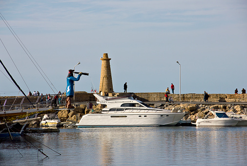 Kyrenia, Cyprus - March 12, 2016: Photo of the waterfront and harbour with sailboats in Kyrenia, Northern Cyprus. People are visiting the harbour for touristic, some of them eating for dinner, some of them are resting near the sea in the Old Harbour in Kyrenia (Girne), Cyprus.