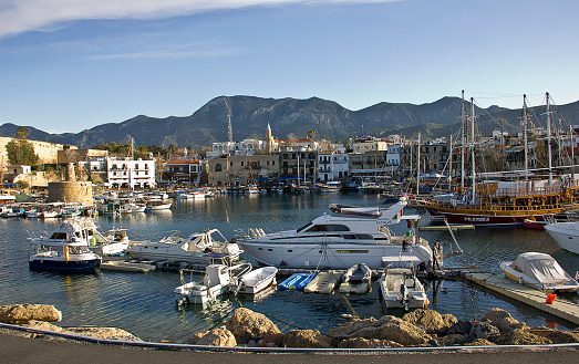 Kyrenia, Cyprus - March 12, 2016: Photo of the waterfront and harbour with sailboats in Kyrenia, Northern Cyprus. People are visiting the harbour for touristic, some of them eating for dinner, some of them are resting near the sea in the Old Harbour in Kyrenia (Girne), Cyprus.