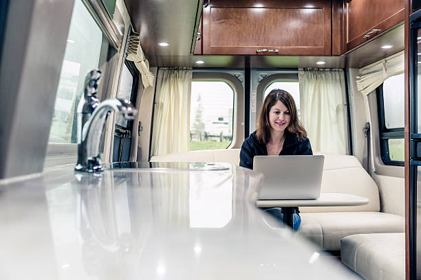 jeune femme à l'aide d'ordinateur portable à l'intérieur de camping-car - motor home park camping luxury photos et images de collection