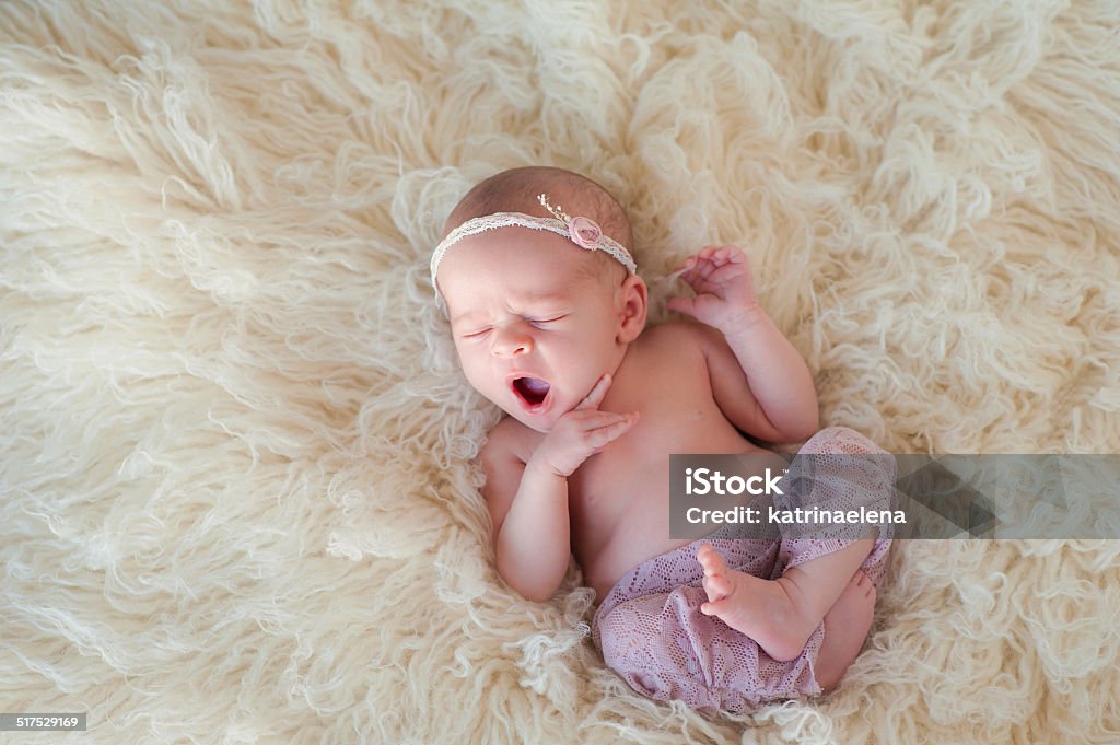 Yawning Newborn Baby Girl Portrait of a yawning 10 day old newborn baby girl. She is curled up and sleeping on her back on a cream colored flokati rug. Babies Only Stock Photo