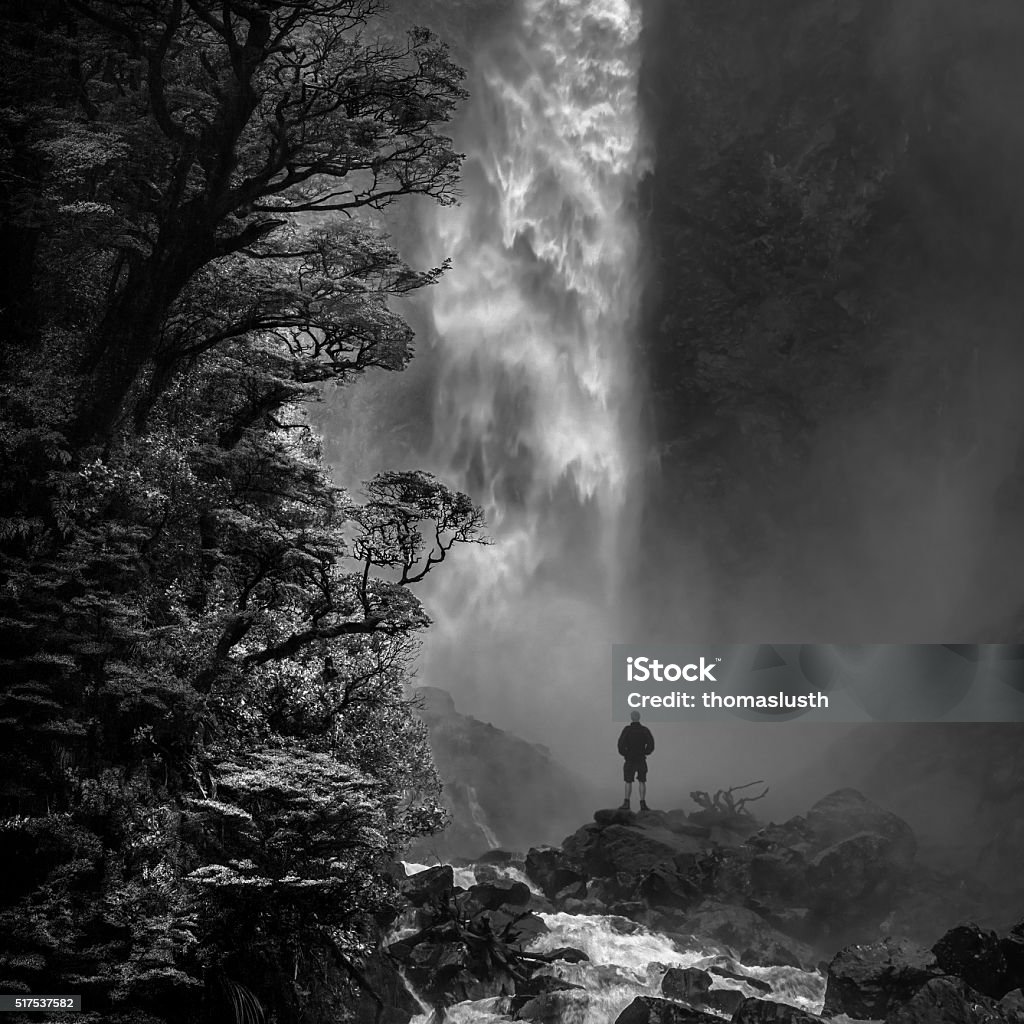 Devil's Punchbowl Man stands in awe in front of Devil's Punchbowl waterfall, Arthur's Pass N.P., New Zealand. Black And White Stock Photo