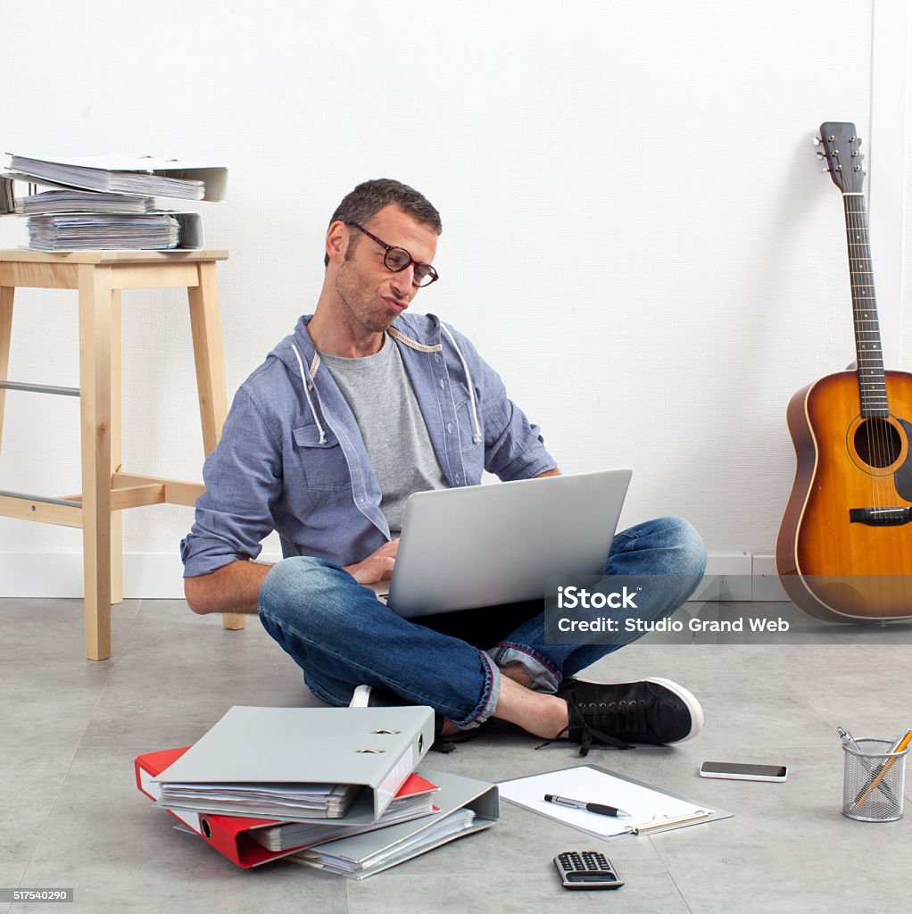 creative start-up entrepreneur working his budget on the floor self-employment concept - creative start-up entrepreneur working his budget sitting on the floor with laptop and paperwork around his home-office 40-49 Years Stock Photo