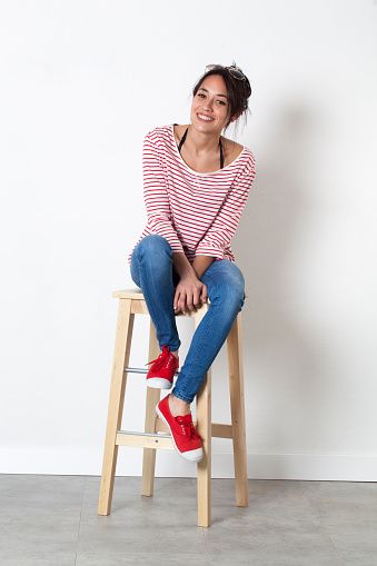 student vacation smile - thrilled beautiful ethnic girl sitting on a stool enjoying free time, white background studio