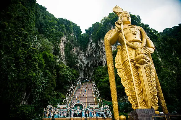 Gold Lord Murugan statue next to the steps leading up to the Batu Caves with limestone in background. Kuala Lumpur, Malaysia.