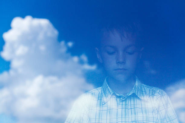 Reflection of a boy and clouds in the window glass.