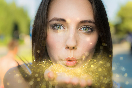 A young woman blowing gold glitter towards the camera.