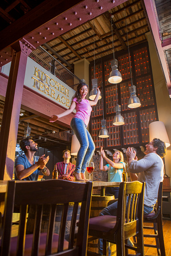 A young asian woman dances on the table in a pub. Her friends cheer her on.