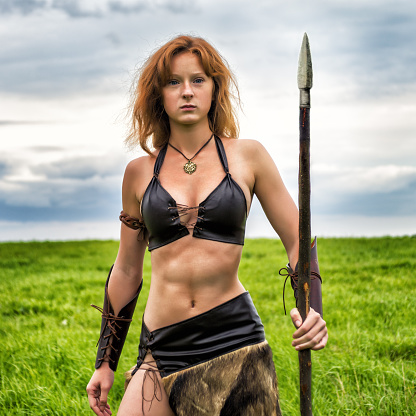 Beautiful red-haired girl in the image of ancient warriors on the background summer nature. Evening.