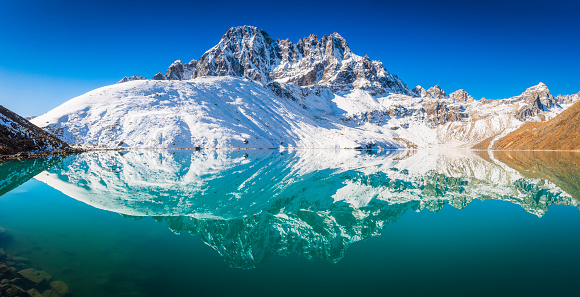 The dramatic rocky pinnacles and snowy summits of Pharilapche (6017m) and the Renjo La remote Himalaya mountain pass reflecting in the tranquil waters of Gokyo Lake deep in the Everest National Park, Nepal, a UNESCO World Heritage Site. ProPhoto RGB profile for maximum color fidelity and gamut.