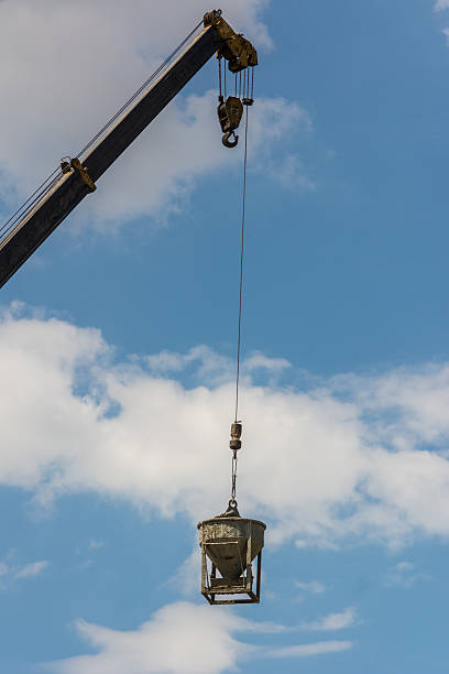 Tower crane lifting cement mixing container, industrial crane hoisting concrete mixing container in inner city with urban infrastructure skyscrapers in the blue sky background