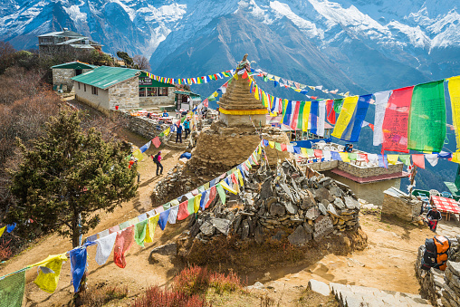 Namche Bazaar, Nepal - November 2, 2014: Hikers trekking past a traditional stupa shrine festooned with colourful Buddhist prayer flags fluttering in the breeze above a collection of Sherpa teahouses and lodges deep in the Himalayan mountains of the Everest National Park, a UNESCO World Heritage Site, Nepal.
