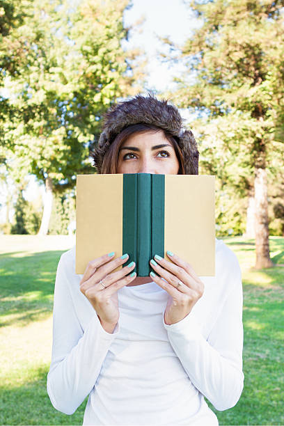 istock Young Woman Hiding Behind a Book 517579115