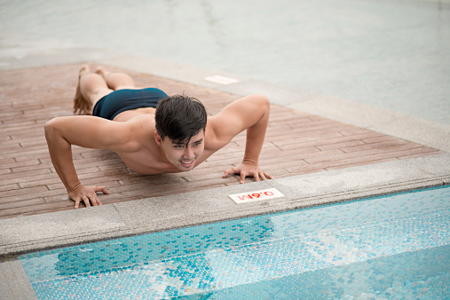 Young man doing push-ups by the swimming pool