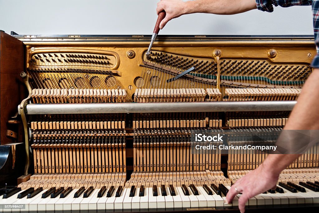 Piano Tuner at Work Colour photo of a piano tuner at work tuning an upright piano. Horizontal format showing the complicated internal workings of a piano, with one hand the man is using a ratchet to tighten or loosen the correct wire to tune the key his other hand is pressing. Piano Tuner Stock Photo