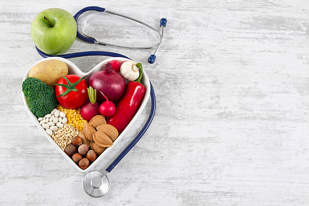 Healthy Foods in Heart Shaped with Stethoscope Heart health, and cholesterol diet concept. Healthy foods in heart shaped bowl with stethoscope and green apple on white vintage wooden table. heart-healthy diet stock pictures, royalty-free photos & images