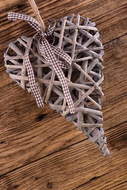 Vertical photo with nice wicker heart with brown bow placed on old wooden board.