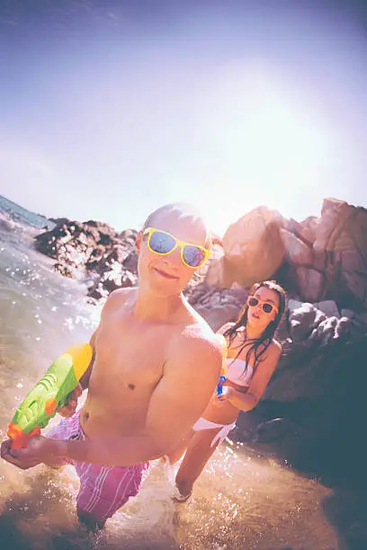 Guy enjoying water fight with water gun at the beach