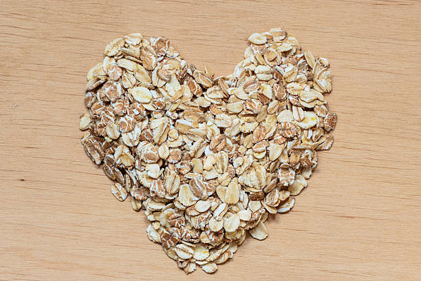 aveia em flocos de cereais em superfície de madeira em formato de coração. - oatmeal breakfast healthy eating cholesterol - fotografias e filmes do acervo