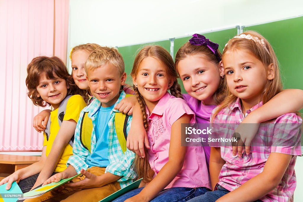 Group of children stand close to each other hug Group of children stand close to each other and hug in front of blackboard and looking straight Backpack Stock Photo