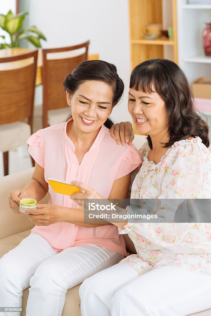 Using smartphone Mature Asian woman showing something on the smartphone to her friend Females Stock Photo