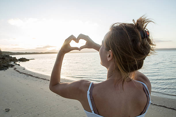 istock Woman on beach makes heart shape finger frame towards sun 517630400