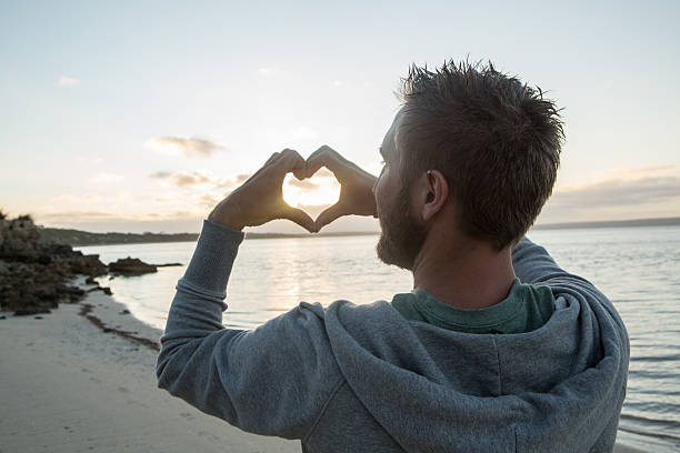 istock Young man on beach makes heart shape finger frame 517632314