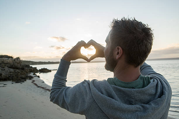 Young man on beach makes heart shape finger frame