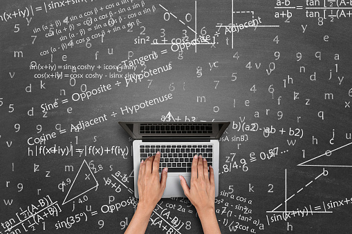 Directly above shot of a woman student using laptop. Concept of online education or e-learning. Math theory and mathematical formula equation written on blackboard.