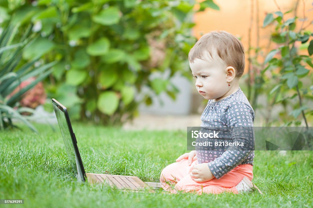 Cute baby girl using a laptop Cute baby girl using a laptop in the garden 12-17 Months Stock Photo