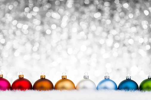 Multicolor clean baubles on the white fur as snow, Defocused light background. Baubles arranged in a single line