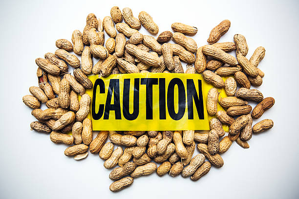 Peanut Allergy Caution A pile of whole peanuts on a white table, yellow caution tape wrapped around them.  Conceptual image representing peanut or other nut allergies.  Horizontal image. food allergies stock pictures, royalty-free photos & images