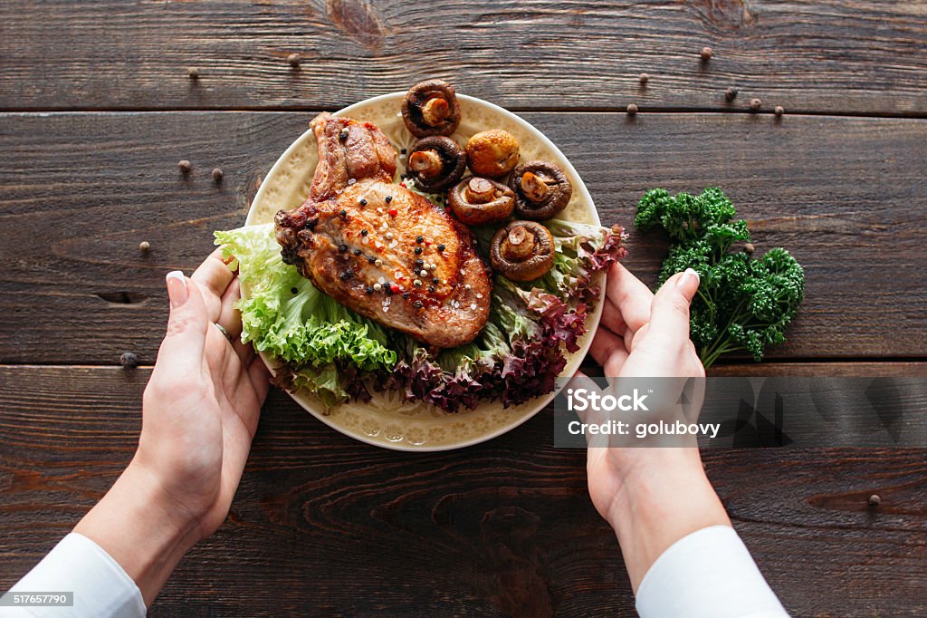 Food serving. Waiter serving a chicken dish. Waiter serving a chicken dish with lettuce and mushrooms. Chief decorating food for presentation in small cafe. Waiter presenting grilled chicken with salad for retail.  Plate Stock Photo