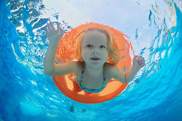 ребенок, плавание в бассейне надувной оранжевой пробкой - inflatable floating on water life belt equipment стоковые фото и изображения