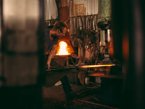 Blacksmith working metal in his forge Young adult caucasian blacksmith is working a metal bar with a mechanical press Furnace stock pictures, royalty-free photos & images